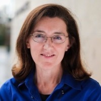 Photo of Jane McNamara Christenson looking at the camera wearing a blue shirt with a light background